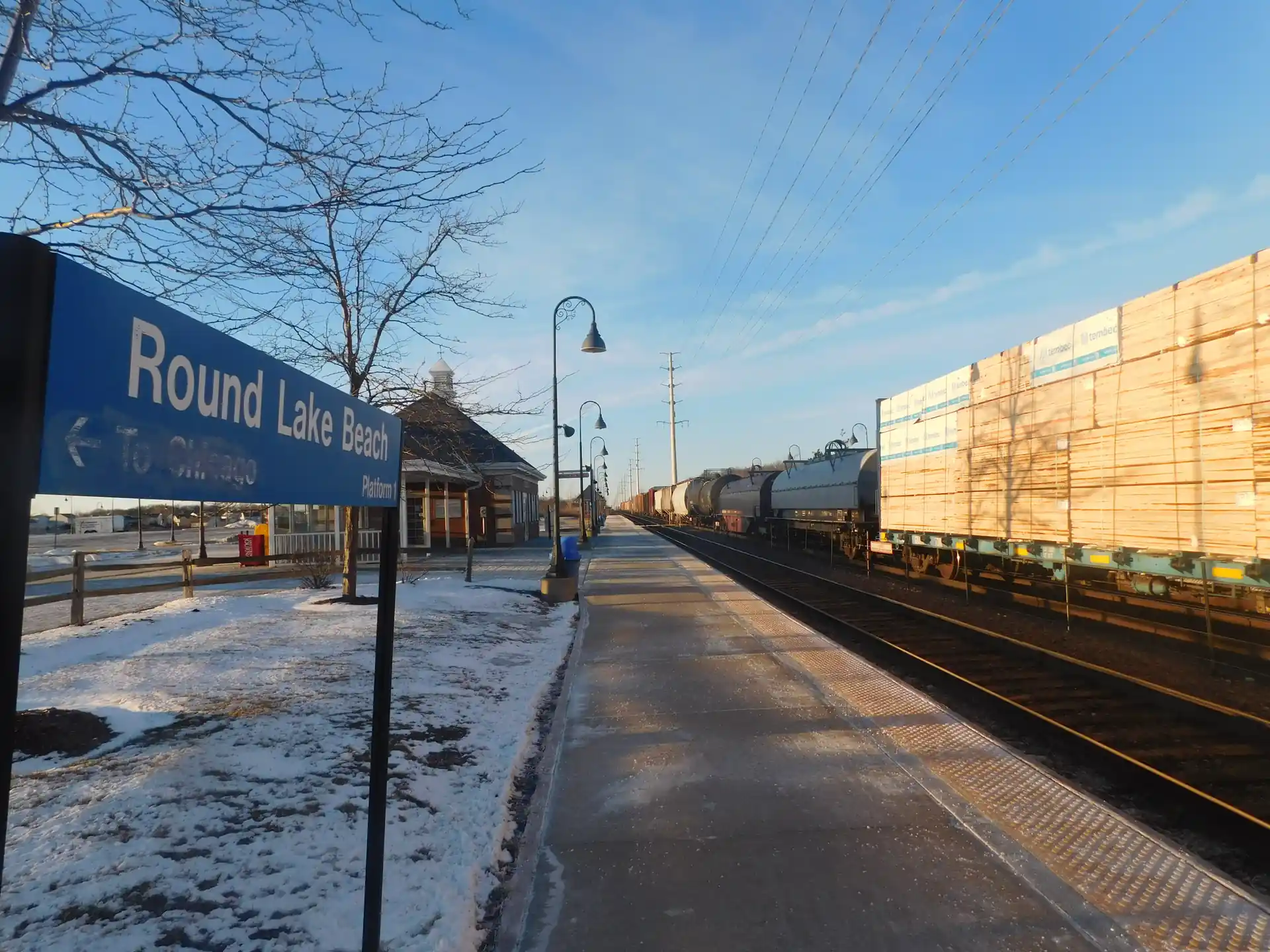 Metra North Central Service station platform in Round Lake Beach, IL, with covered waiting area and station sign